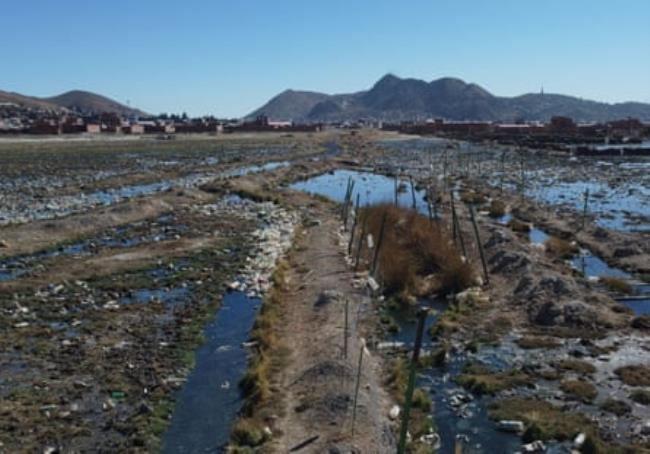 A watery ditch filled with plastic bottles and other rubbish with a settlement in the background